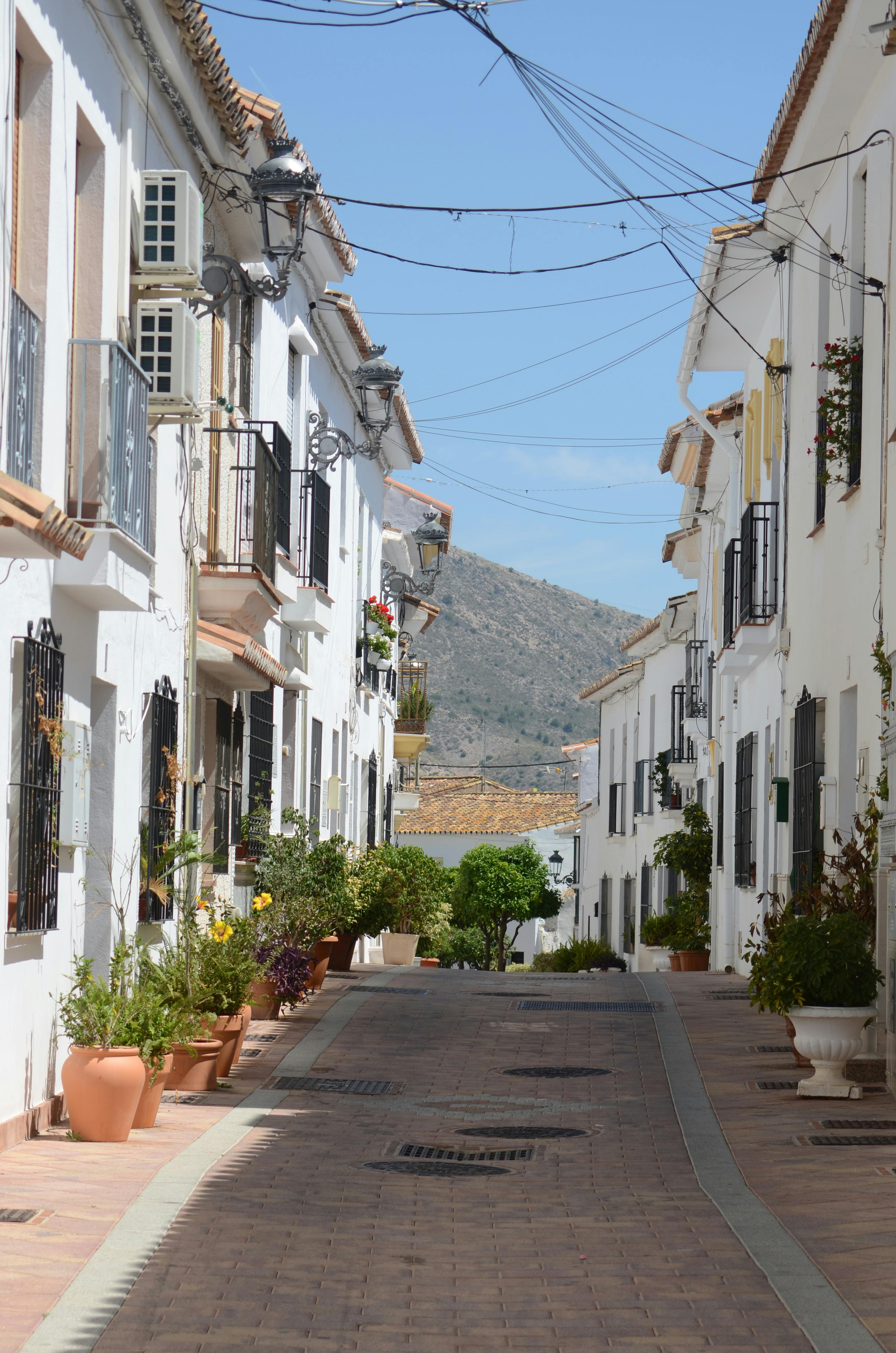 Charming narrow street lined with whitewashed houses and colorful flowerpots in Benalmádena Pueblo old town.