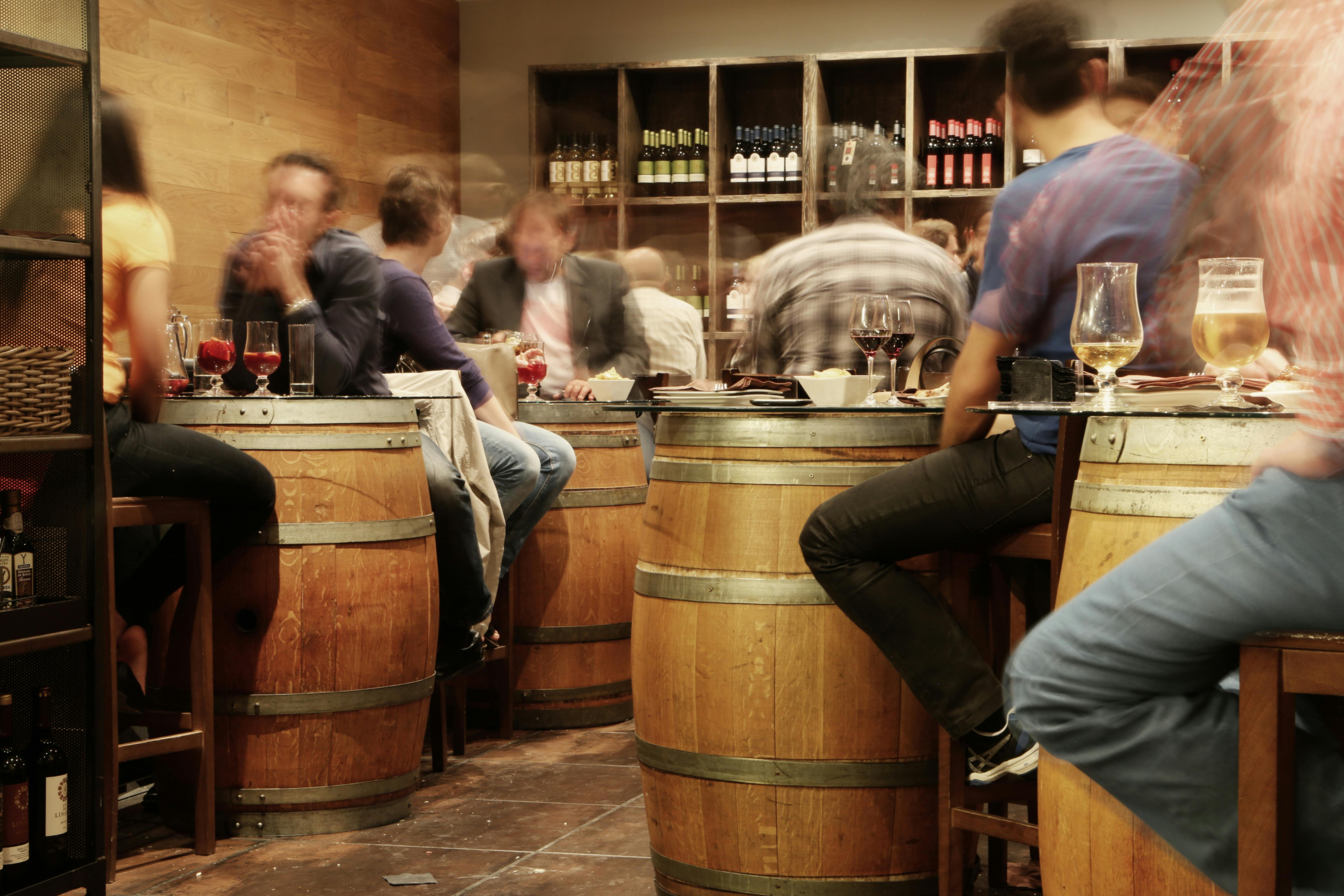 A bustling interior of a traditional Spanish taberna along the Costa del Sol, featuring wooden wine barrels used as standing tables, hanging jamón, and people enjoying authentic tapas.