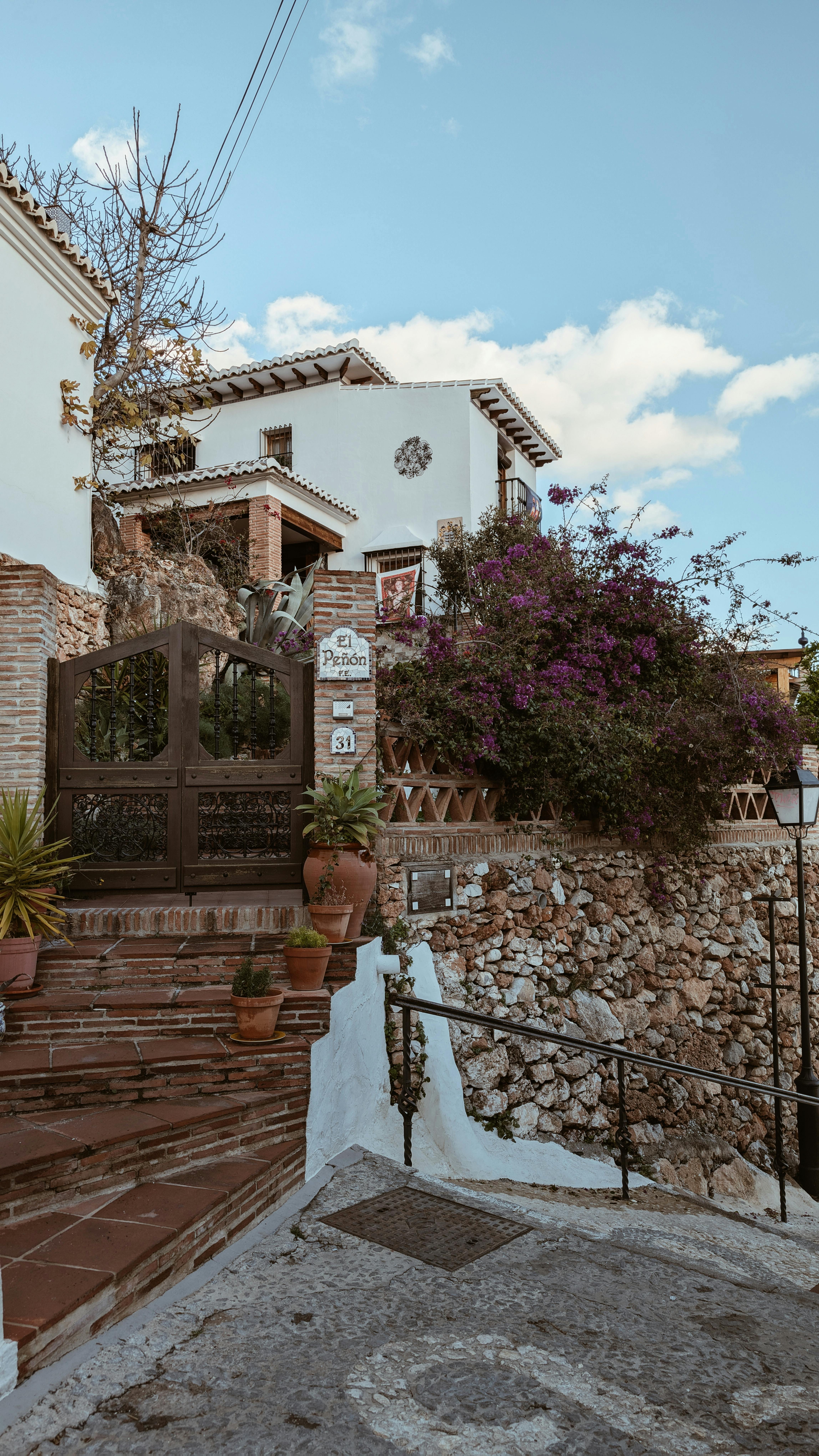 Traditional whitewashed house in Nerja pueblo decorated with blue flowerpots and pink bougainvillea