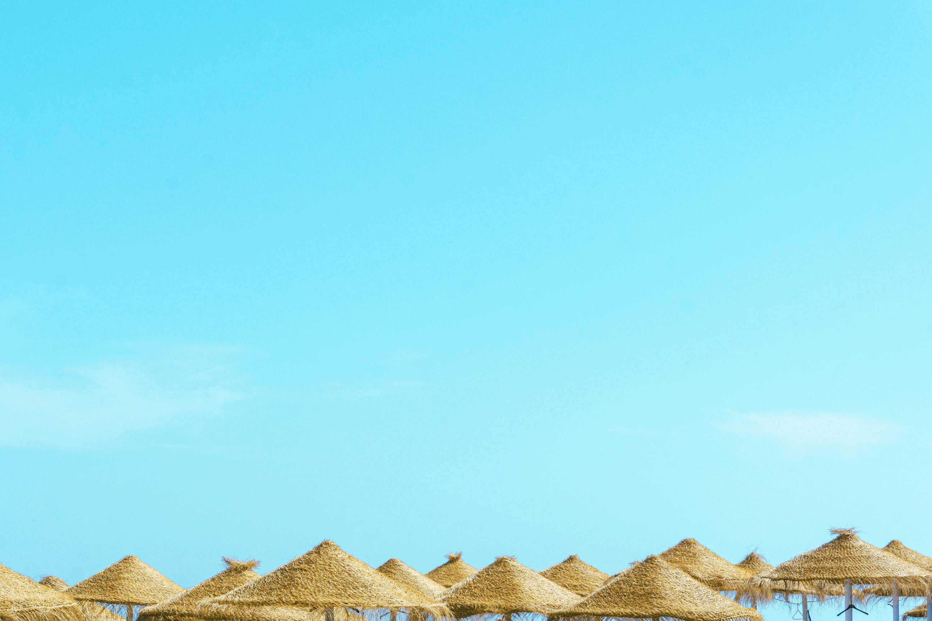 Traditional straw sun umbrellas against a clear blue sky on a beach in Costa del Sol.