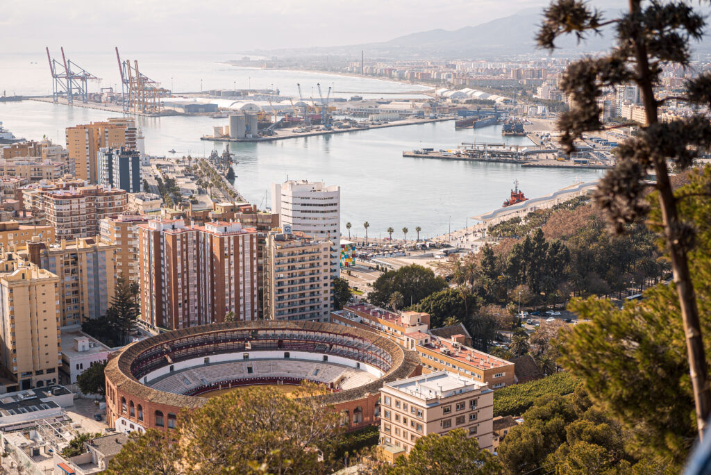 Panoramic aerial view of the Málaga city skyline, showcasing the historic center, the cathedral, and the modern harbor fronting the Mediterranean Sea.