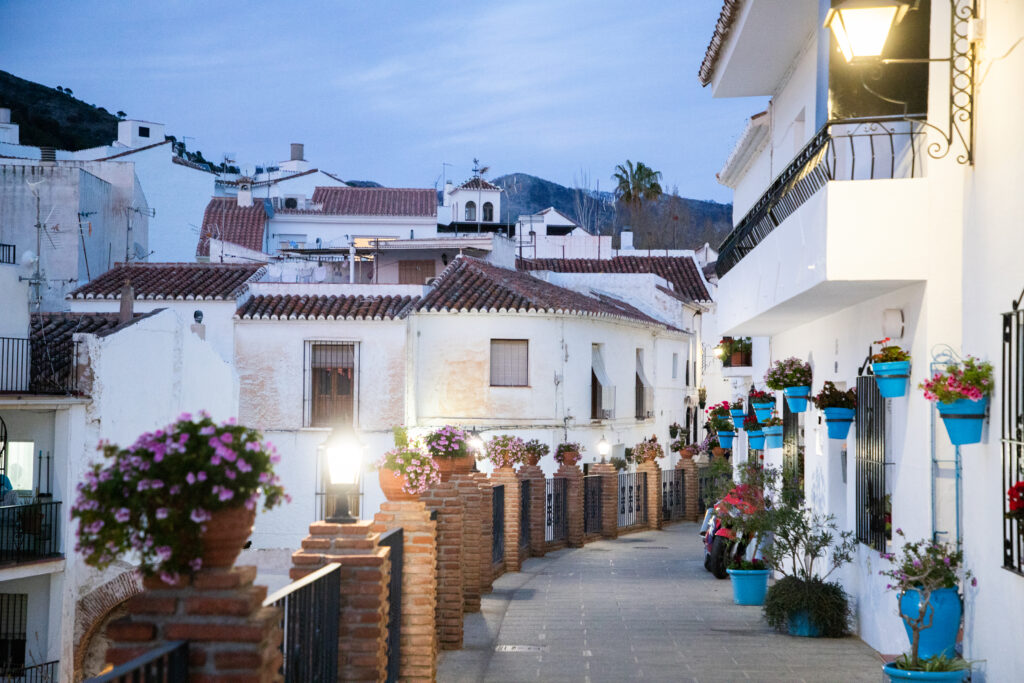 A narrow street in Mijas Pueblo lined with traditional blue flower pots hanging on white walls.