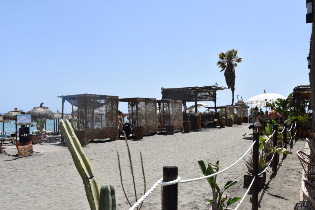 Open-air beachfront chiringuito restaurant with thatched umbrellas and outdoor seating along the Mediterranean coast of the Axarquia region in Andalusia.