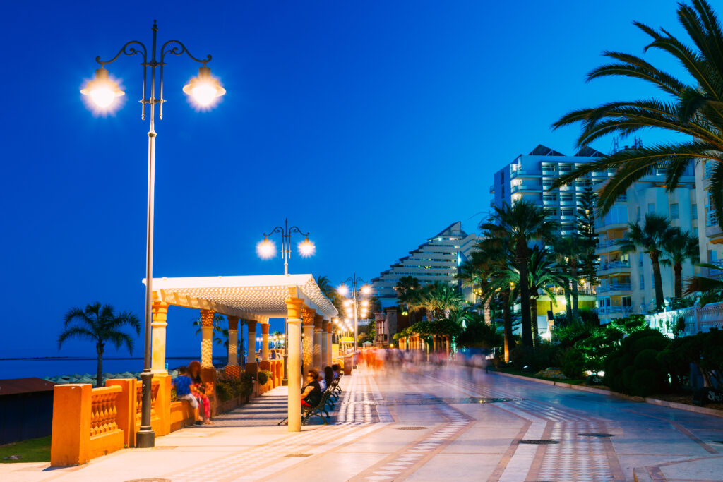 Night view of the illuminated beach promenade, coastline, and sandy beach in Benalmadena, Costa del Sol, Spain.