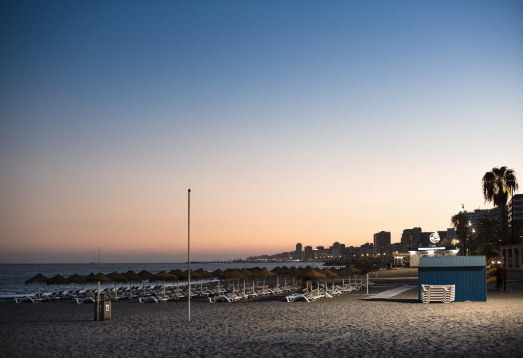 Empty sunloungers and straw umbrellas on a sandy beach at sunset in Fuengirola, Costa del Sol, Spain.