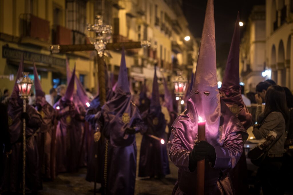 Penitents (Nazarenos) in purple robes and capirotes holding candles during a nighttime Holy Week procession in Andalusia