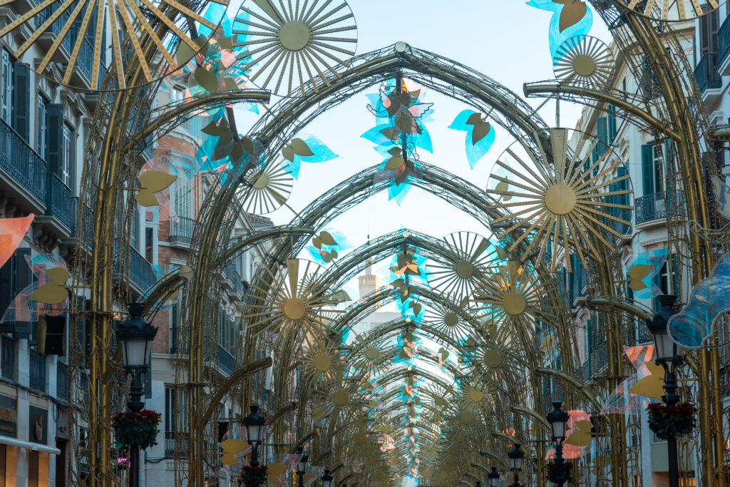 Ornate metallic arches and decorative holiday light structures spanning across Calle Larios in Malaga during the daytime