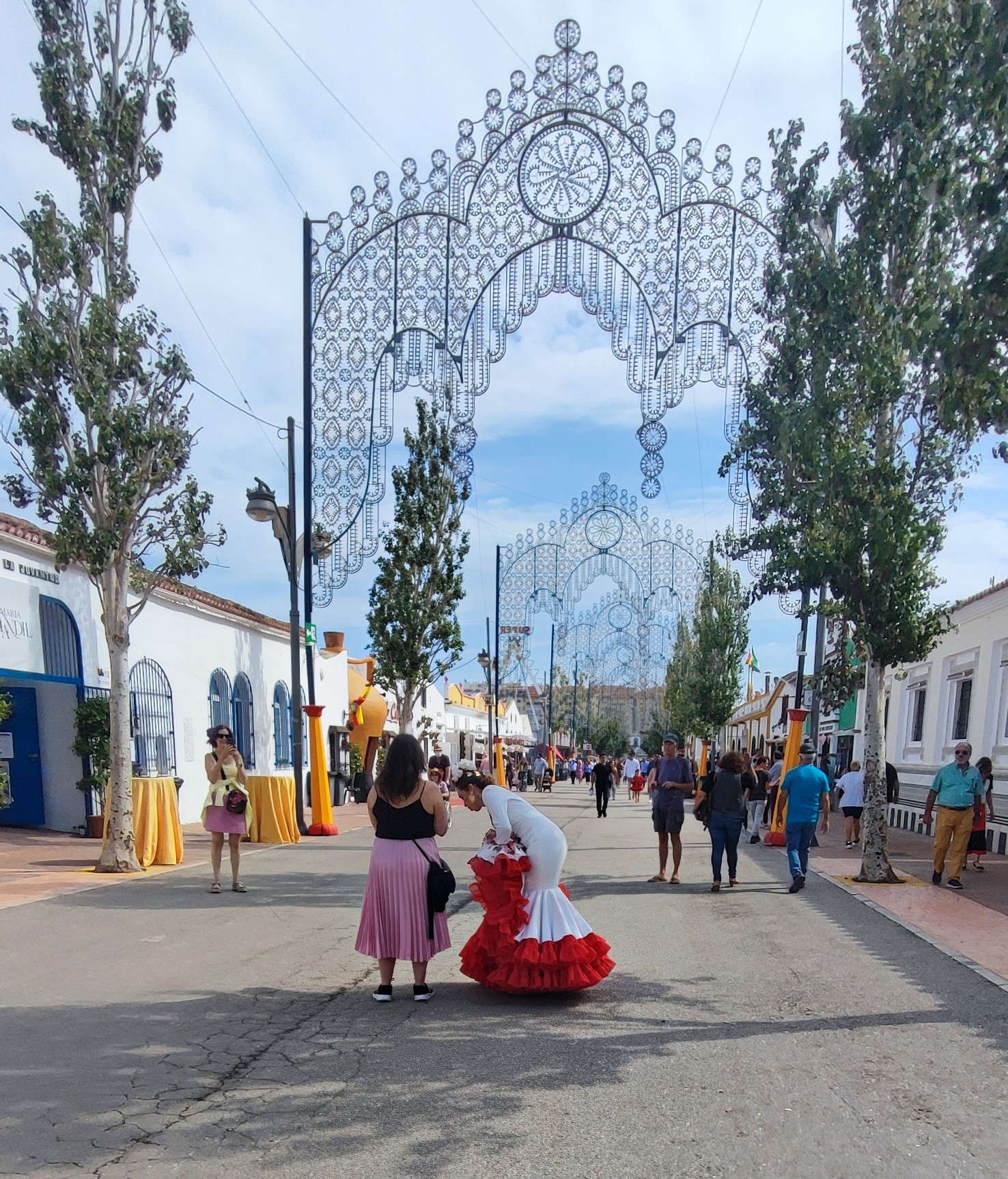 Local women in traditional ruffled flamenco dresses walking through the fairground under decorative light arches at the Fuengirola Feria