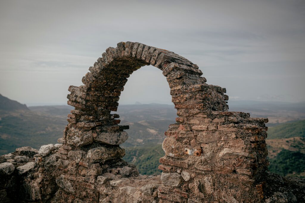 Weathered stone archway ruins on a hilltop overlooking scenic rolling hills and countryside.